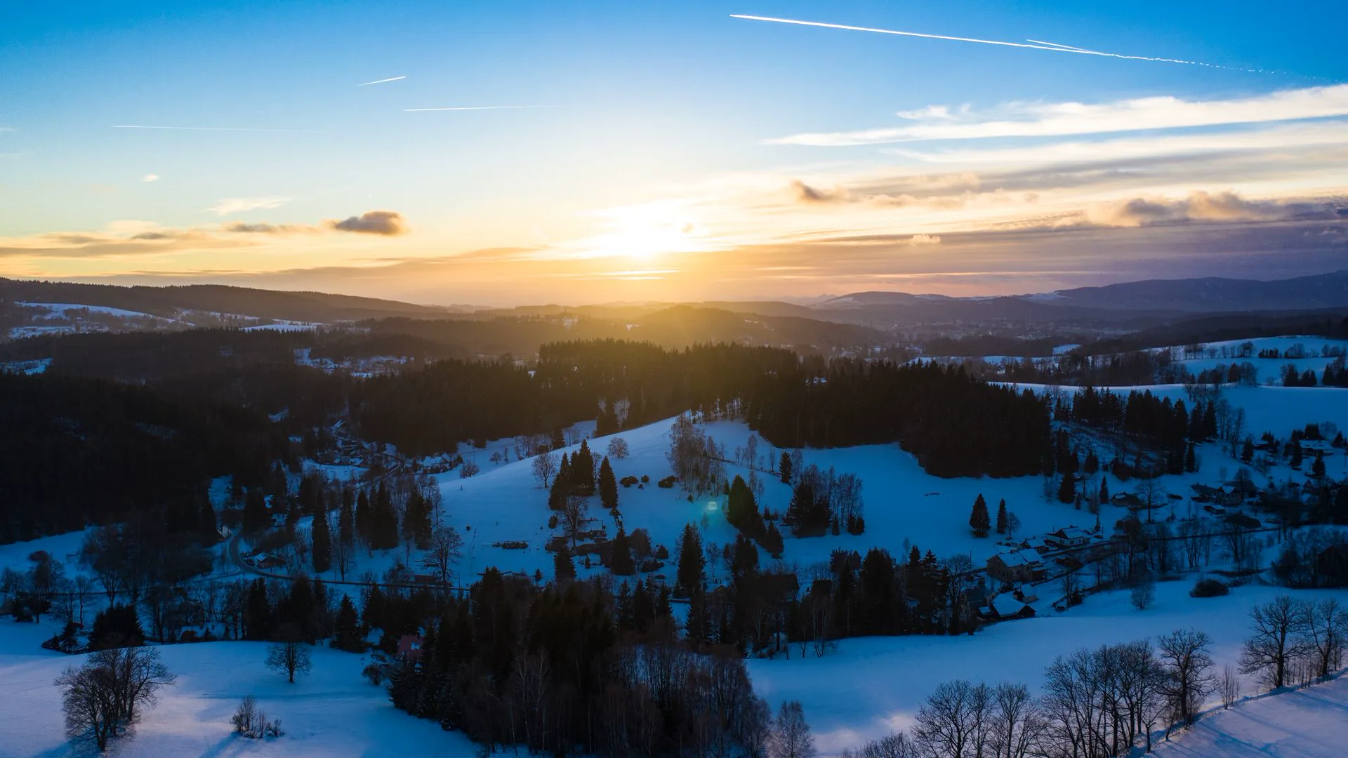 Zasněžená vesnice a kopce při západu slunce (foto z dronu)